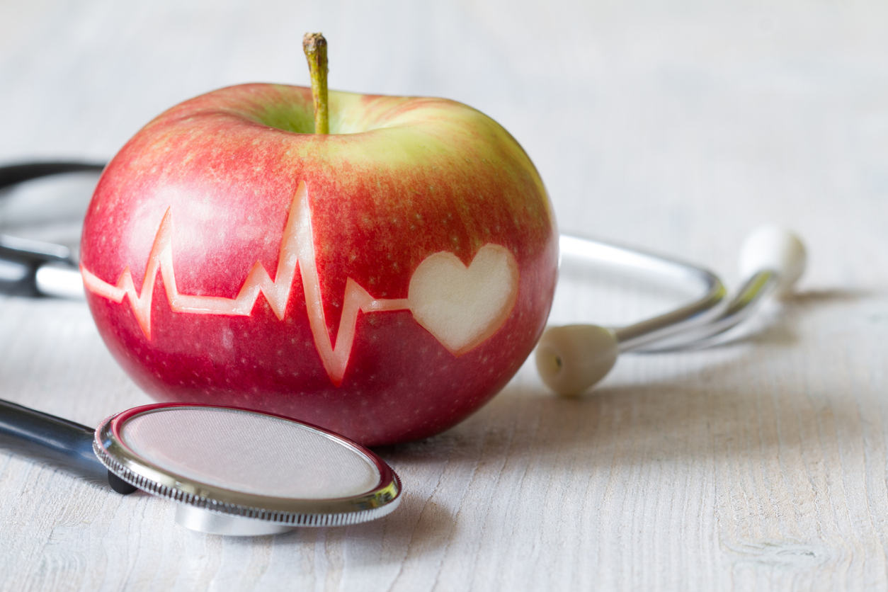 Heartbeat line on an apple and a stethoscope representing the link between heart health and obesity.