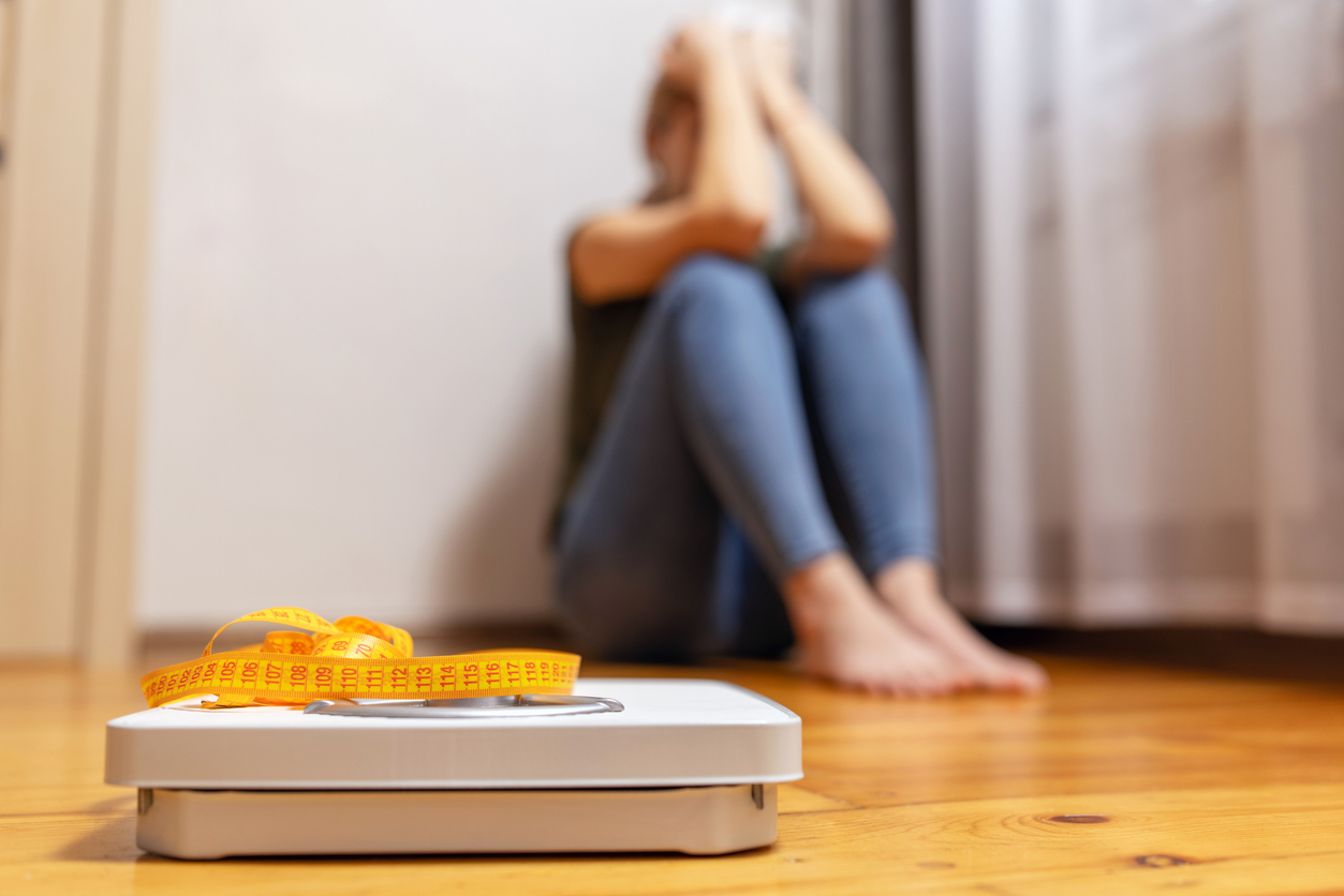 A woman sits on the floor in frustration after bariatric surgery, feeling stressed out about her weight loss journey.