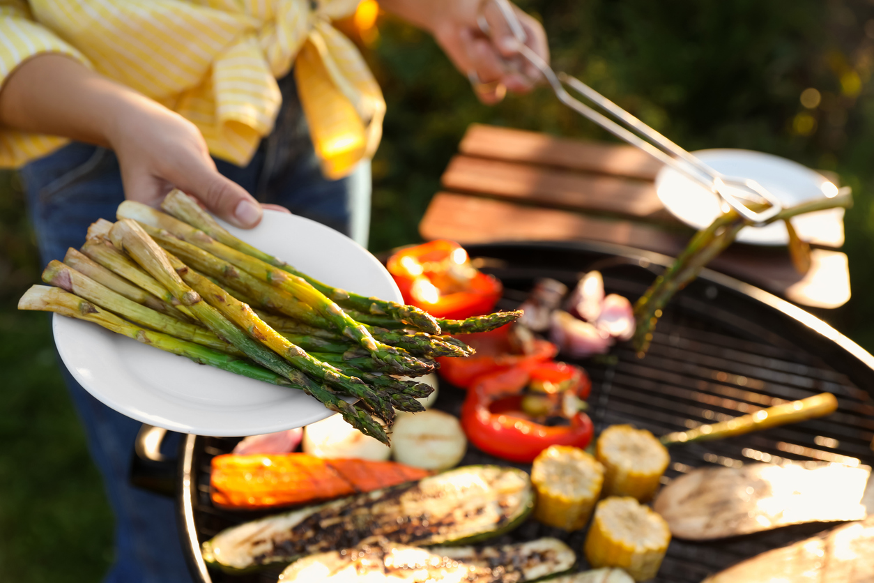 People gathering for a summer barbecue around a grill with healthy food choices