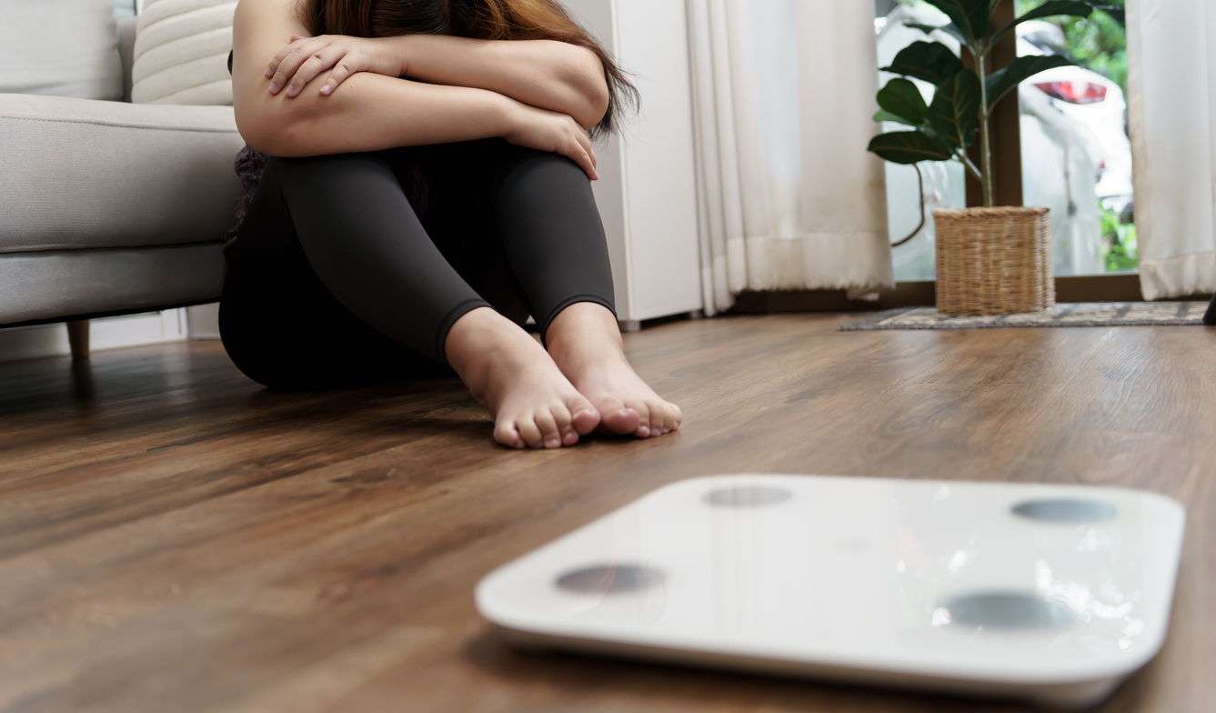 A woman sits far from her scale as she deals with negative body image post-bariatric surgery