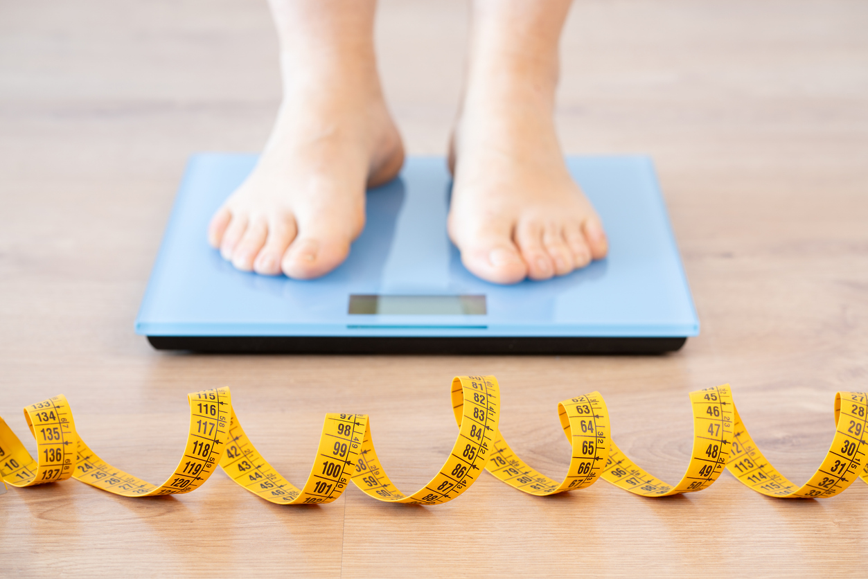 A pair of feet on a scale behind a yellow tape measure, representing childhood obesity and weight loss. 