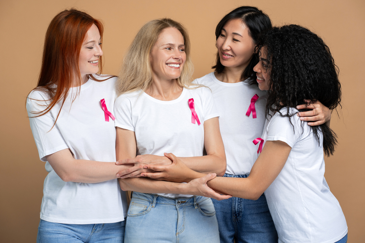 A group of diverse women showing support to each other and wearing breast cancer awareness month ribbons. 